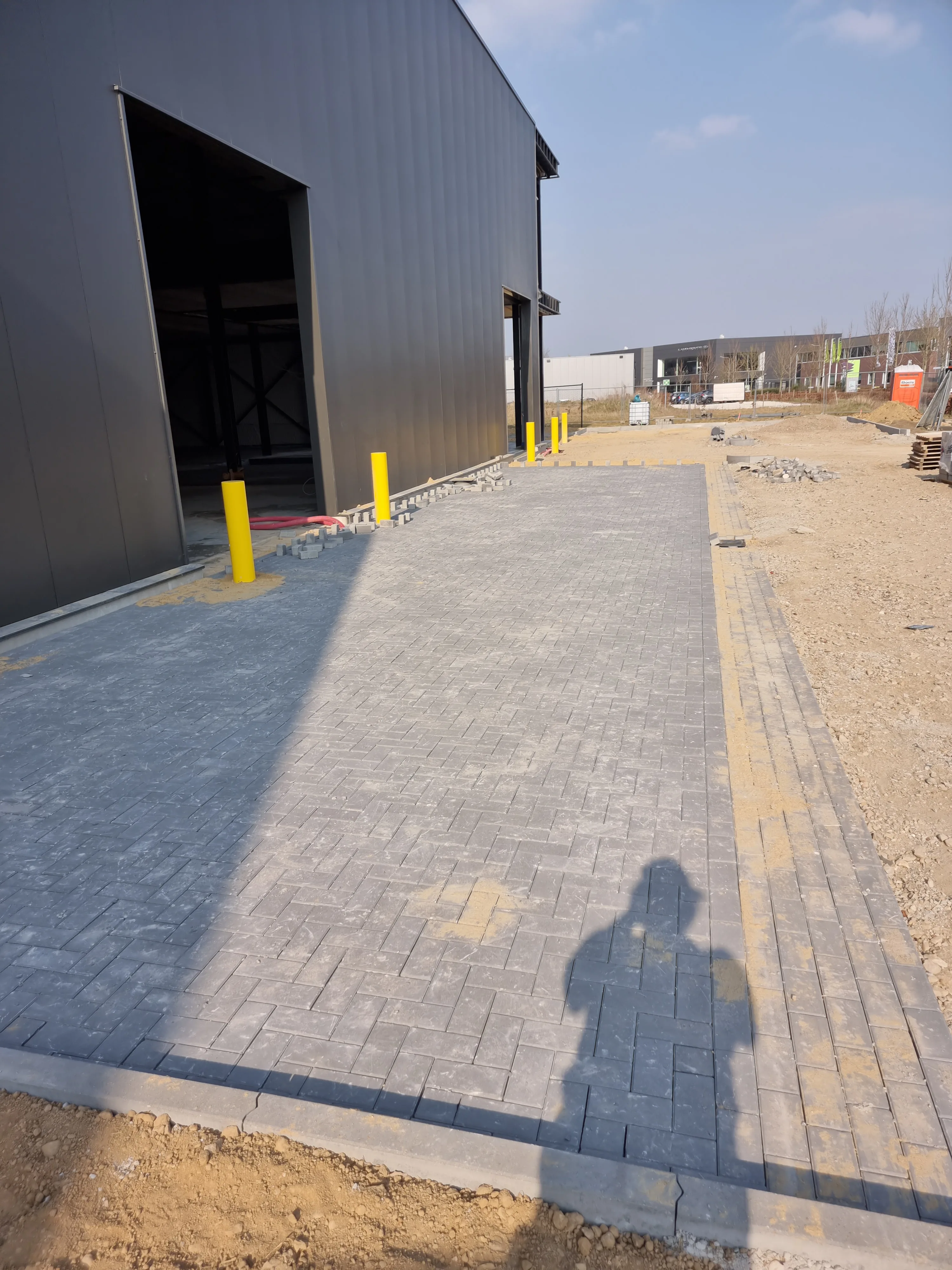 Professioneel parkeerterrein met betonklinkerbestrating, witte markeerlijnen en gele paalbescherming bij magazijn