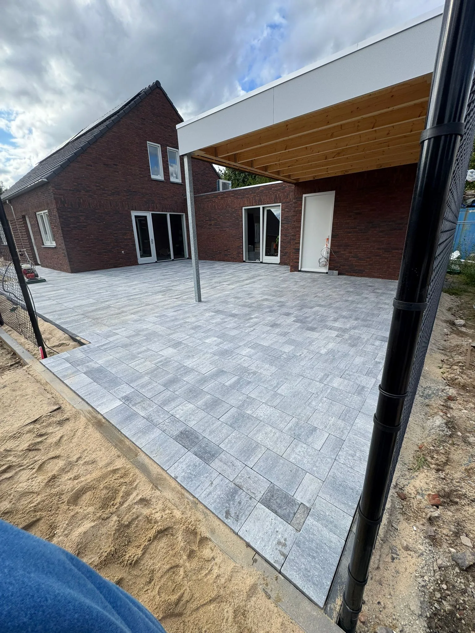 Terras aanleggen: grijze betonklinkers in schaakmotief rond rood bakstenen huis