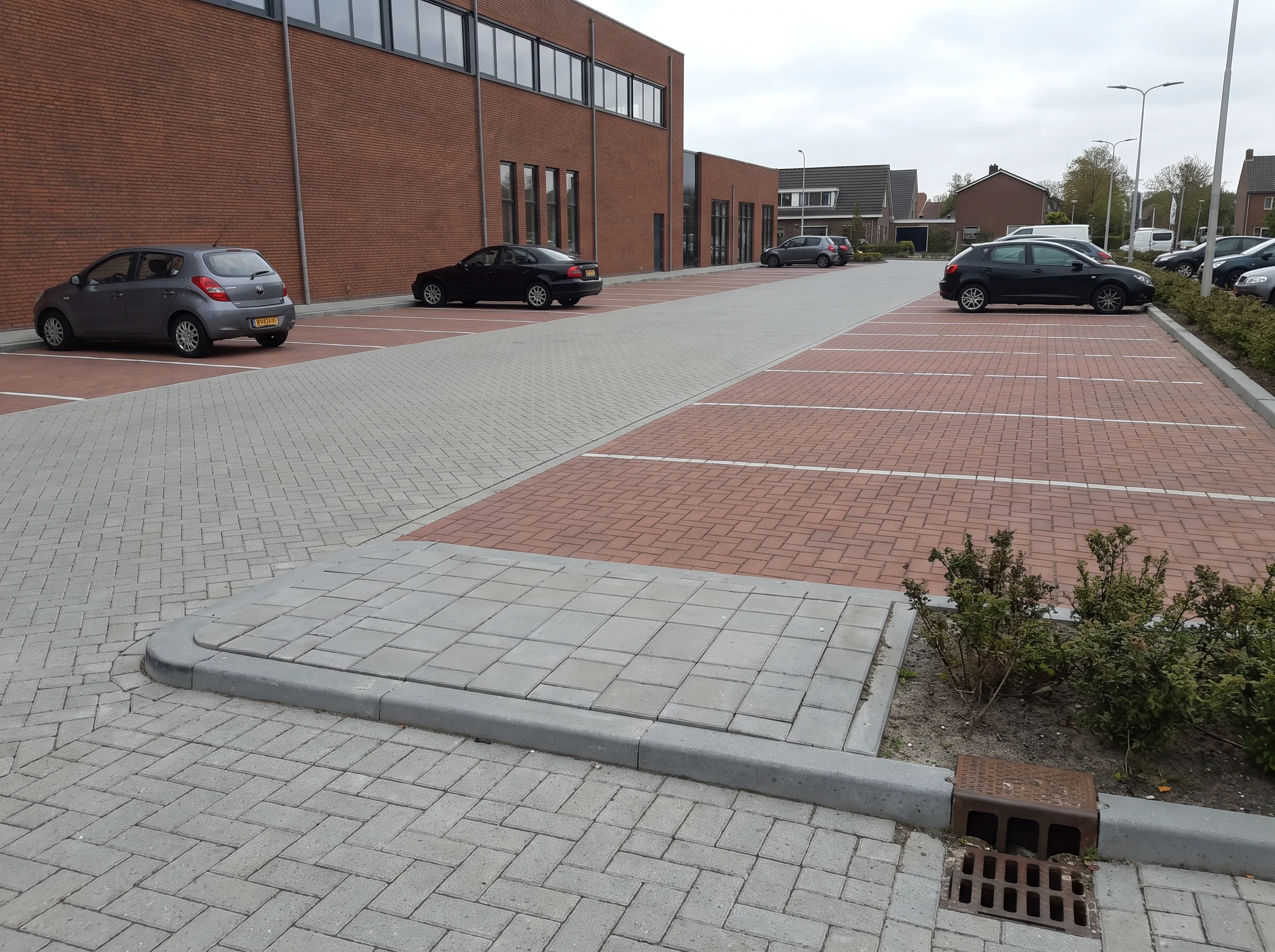 Parkeerterrein met grijze en rode klinkerbestrating, voertuigen en bakstenen bedrijfsgebouw