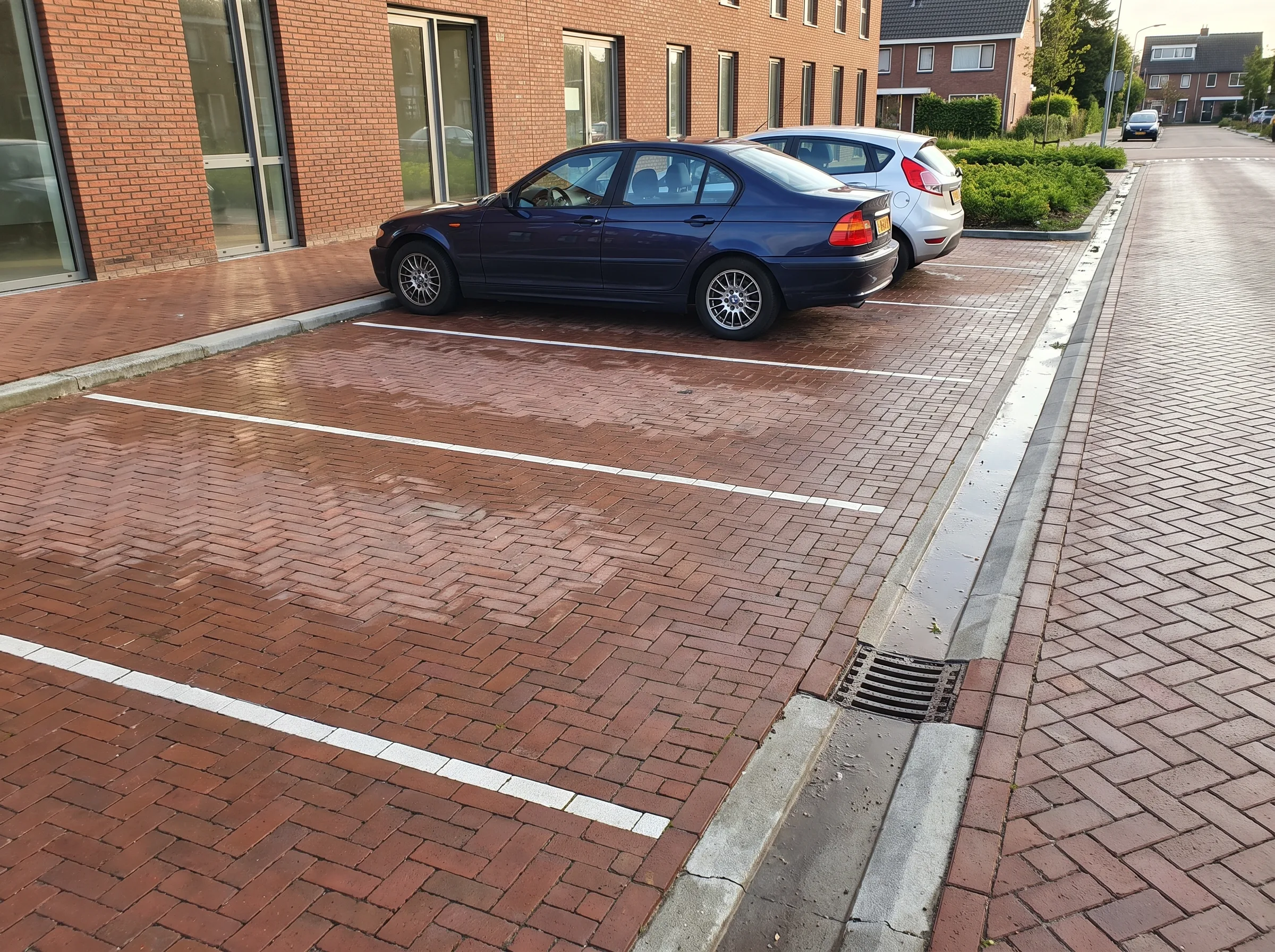 Bestrate parkeerplaats met rode klinkers, witte lijnen en parkeerplaatsen met geparkeerde auto's