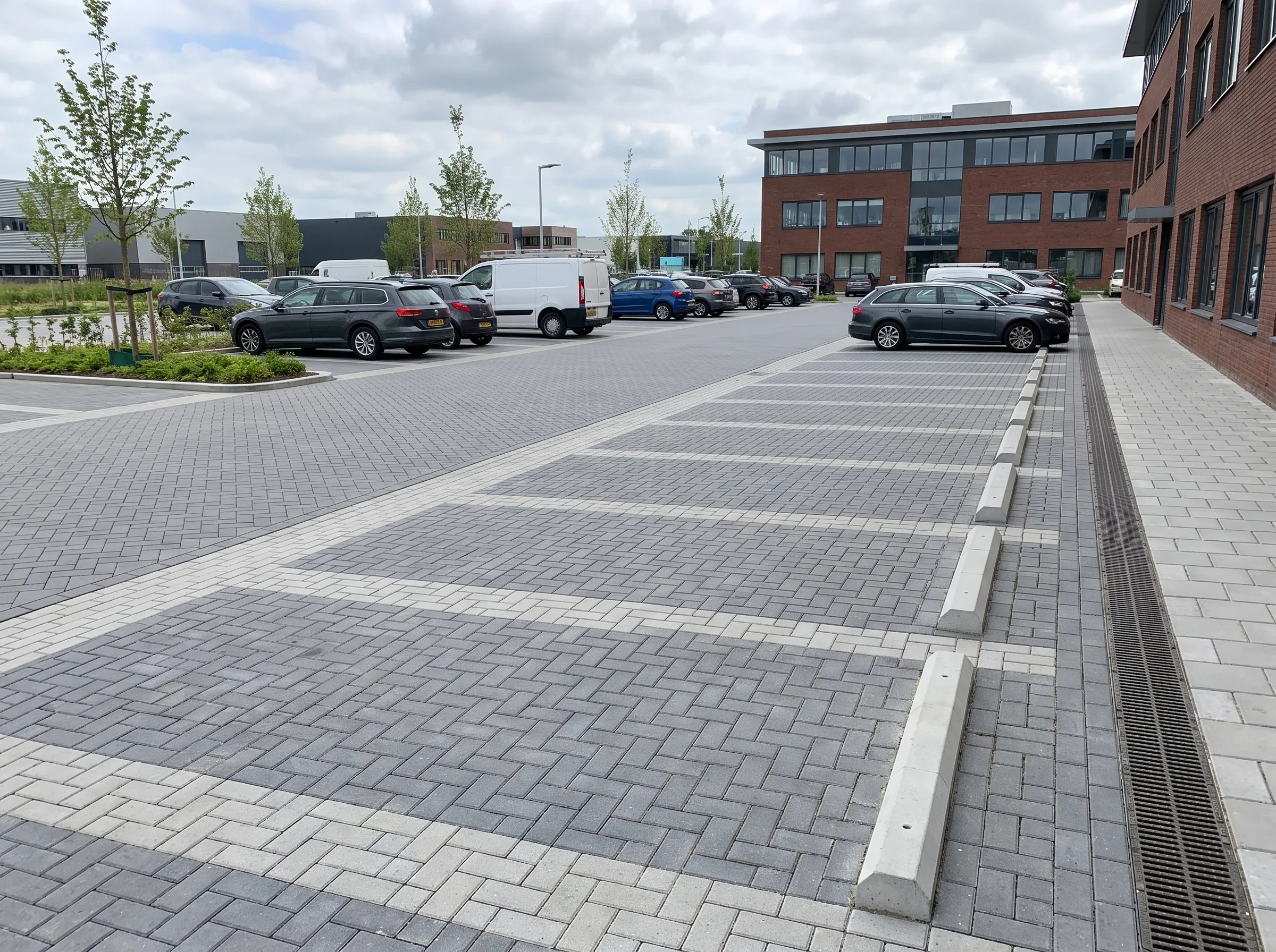 Parkeerterrein met grijze klinkerbestrating in geometrisch patroon, witte opsluitbanden en drainage