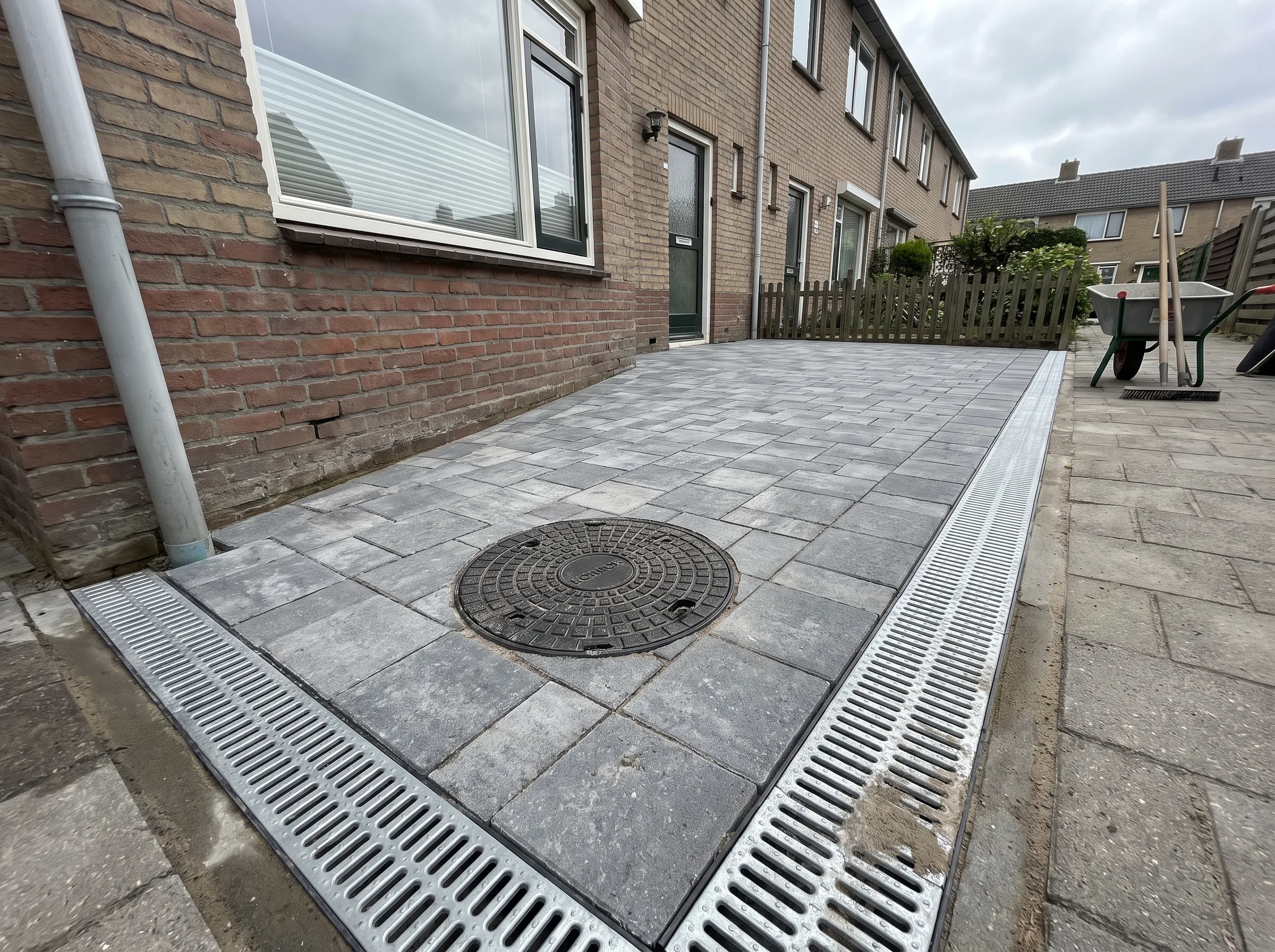 Grijze klinkerbestrating terras met drainagekanalen tegen woning