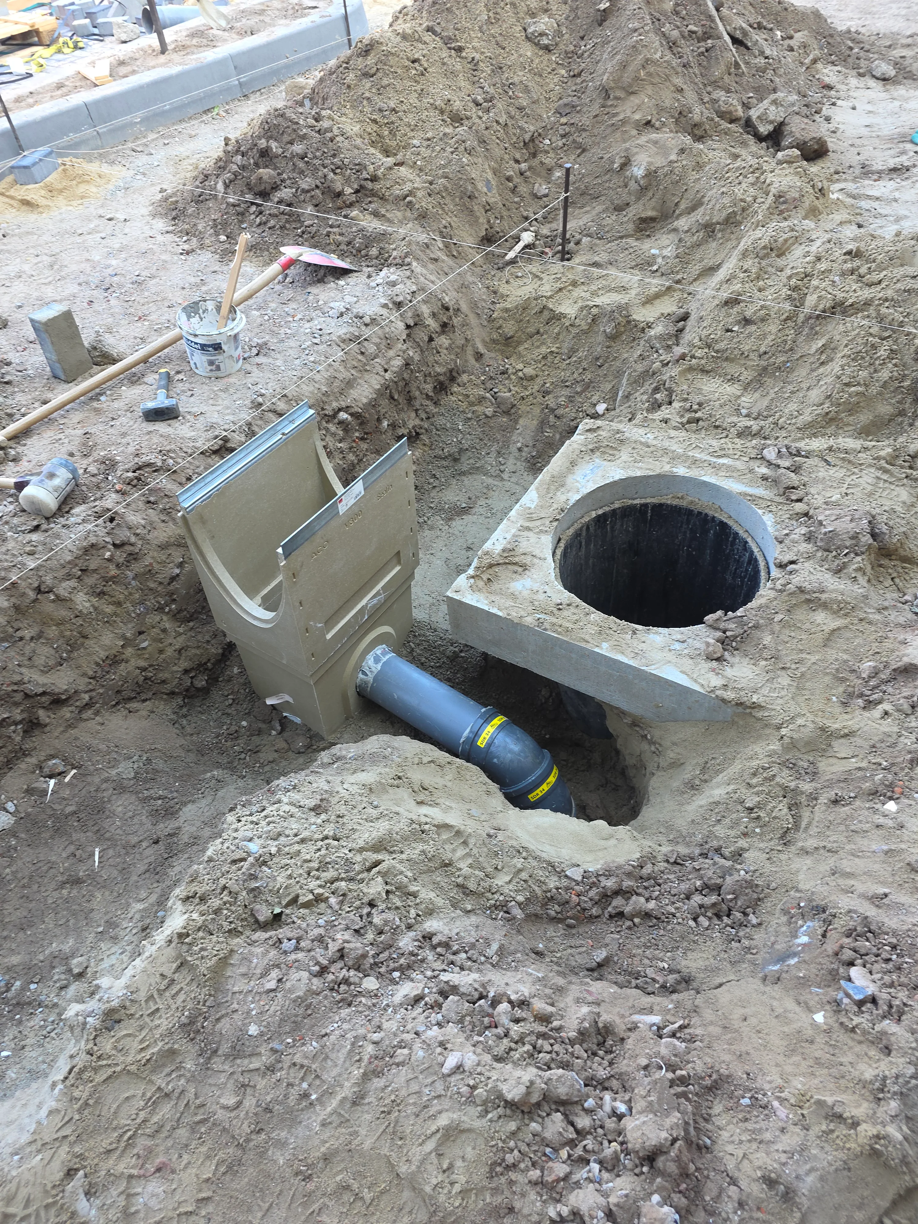 Grondwerk met betonnen inspectiekuil en blauwe drainagepijp tijdens aanleg riolering