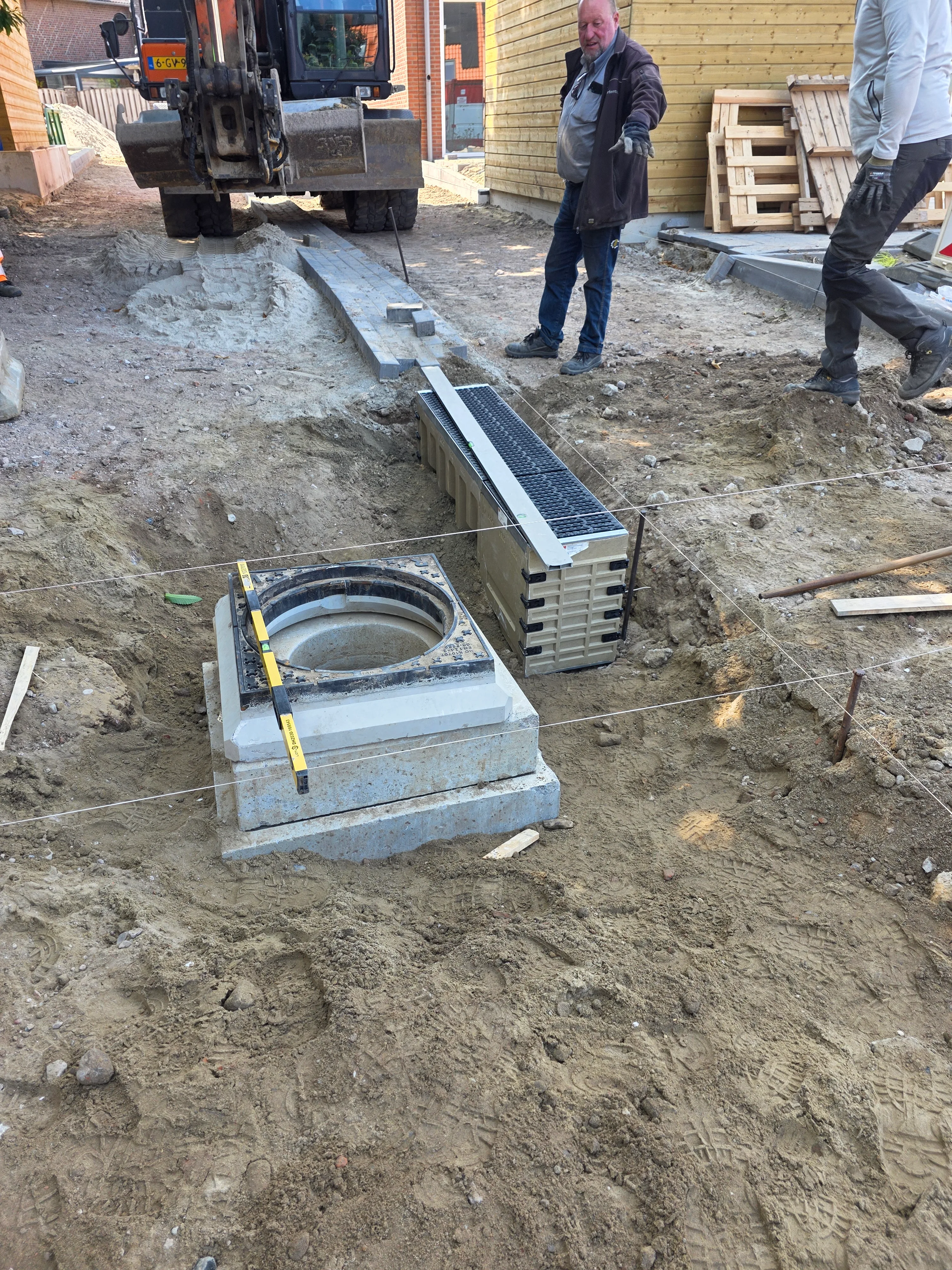 Aanleg drainagesysteem: betonnen inspectieput met roosters en drenagebuizen in graafwerk